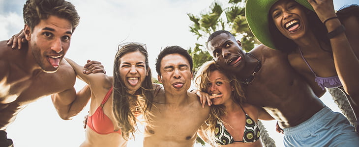 A group of young adults smile and embrace for a selfie on a beach