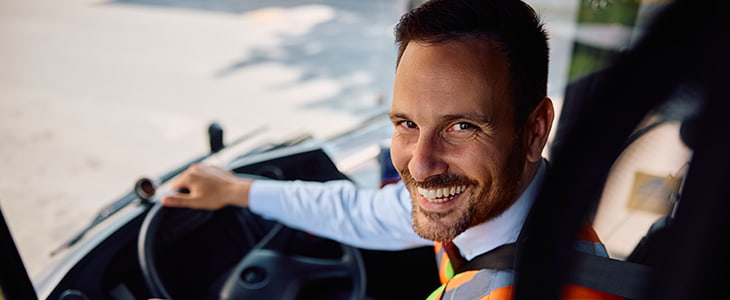 A bus driver smiles over their shoulder at the camera