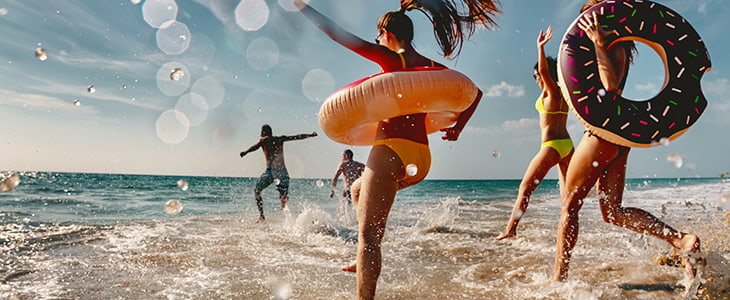 Young people run into the ocean in swimsuits with floating tubes