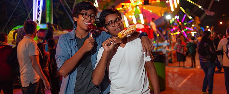 Two teens walk around a nighttime fair with food in hand