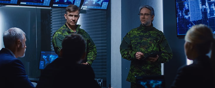 Two military officers present information to a counsel in a meeting room