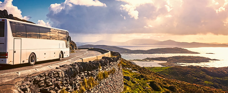 A charter bus drives on a rocky shoreline